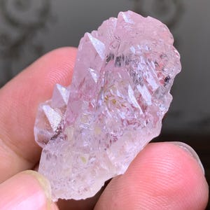 May include: A cluster of light pink quartz crystals with sharp, pointed terminations. The crystals have a translucent quality, with subtle variations in color and texture. The overall shape is irregular and natural, showcasing the raw beauty of the mineral.