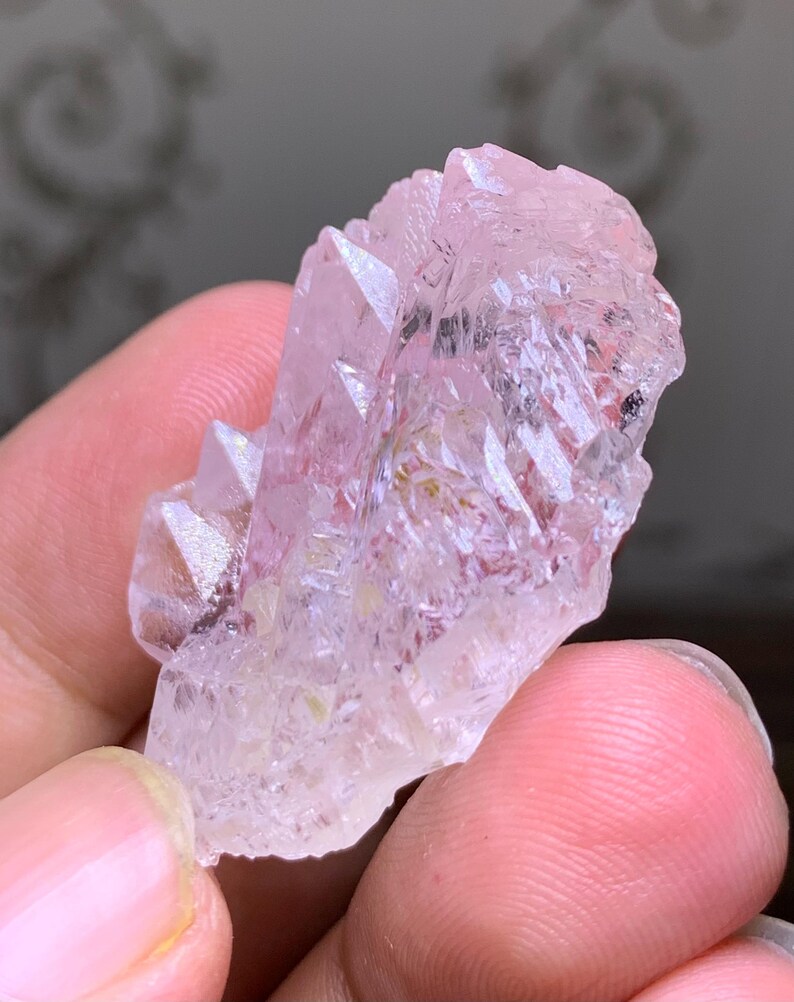 May include: A cluster of light pink quartz crystals with sharp, pointed terminations. The crystals have a translucent quality, with subtle variations in color and texture. The overall shape is irregular and natural, showcasing the raw beauty of the mineral.