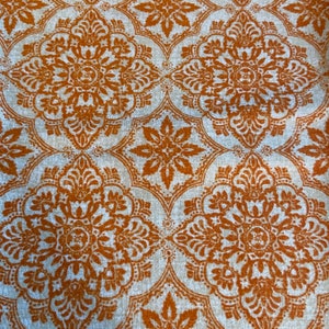 May include: A white fabric with a repeating pattern of orange floral designs. The fabric has a subtle texture.