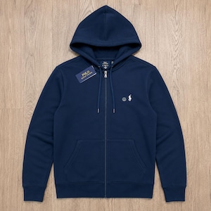 Może przedstawiać: Granatowa bluza z kapturem zapinana na zamek z troczkami. Posiada małe białe logo na piersi i metkę "POLO Ralph Lauren". Bluza ma przednią kieszeń i zamek błyskawiczny na całej długości.