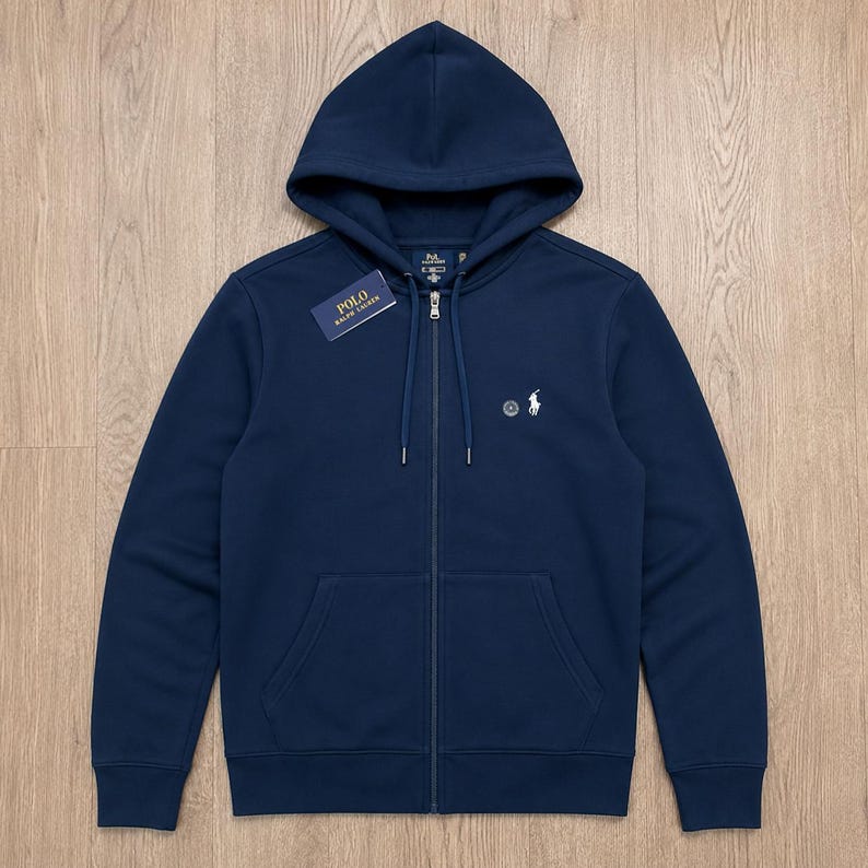 Może przedstawiać: Granatowa bluza z kapturem zapinana na zamek z troczkami. Posiada małe białe logo na piersi i metkę "POLO Ralph Lauren". Bluza ma przednią kieszeń i zamek błyskawiczny na całej długości.