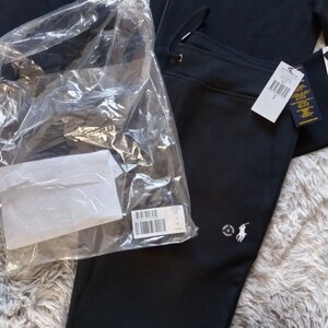 May include: Black tracksuit set, including a zip-up hoodie and sweatpants. The hoodie features a small logo on the chest, and the sweatpants have a matching logo. The set is new, with tags still attached and packaged in plastic.