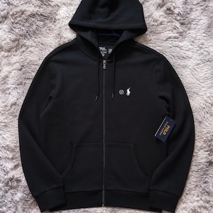 May include: Black zip-up hoodie with a hood and front pockets. Features the Polo Ralph Lauren logo on the chest and a tag on the lower right. The hoodie has a full zipper and a drawstring hood.