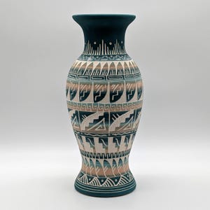 May include: A tall, decorative vase with a dark teal rim and base. The body features intricate geometric patterns in shades of teal, beige, and brown. The vase has a wide body and a slender neck, showcasing a Southwestern design.