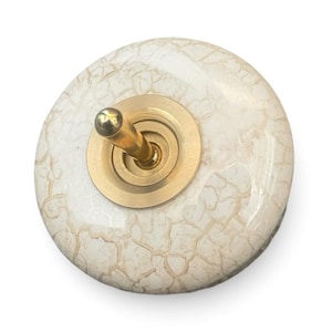 May include: A white ceramic light switch with a gold metal toggle and a crackled glaze finish.