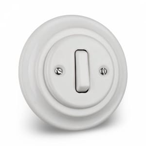 Op de afbeelding: Een witte, ronde keramische lichtschakelaar met een rechthoekige tuimelschakelaar. Het ontwerp is klassiek met een verhoogd, cirkelvormig frame en twee kleine schroeven. De schakelaar staat uit.