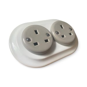 May include: A white electrical outlet with two gray receptacles. The outlet has a rounded, oval shape and is designed for electrical plugs. The receptacles have three holes for the prongs of the plug.