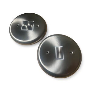 May include: Two brushed nickel light switch covers. One with two switches, the other with one. Each round cover has screw holes either side of the switches. The switches are white.
