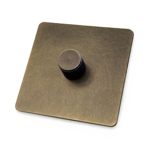 Op de afbeelding: Een vierkante, antieke messing dimmer schakelaar met een ronde, zwarte knop.