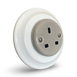 May include: A white, round electrical outlet with a gray center. The outlet has three rectangular holes and a single vertical slot. Two screws secure the gray center to the white base. The outlet is designed for electrical use.