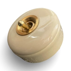 May include: A cream-colored ceramic light switch with a gold-toned toggle and trim.