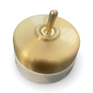 May include: A gold light switch with a white ceramic base. The switch has a round, flat design and a single toggle.
