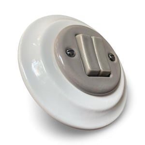 May include: A white ceramic light switch with a grey centre and two grey toggle switches. The switch is mounted on a round base and secured with two small screws. The design is a classic, vintage style.