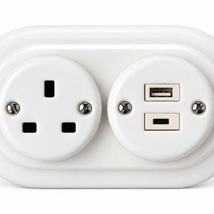 May include: A white dual-outlet wall plate featuring a standard three-pin electrical socket on the left and a combination USB-A and USB-C charging port module on the right, secured by two visible metal screws on each circular faceplate section.