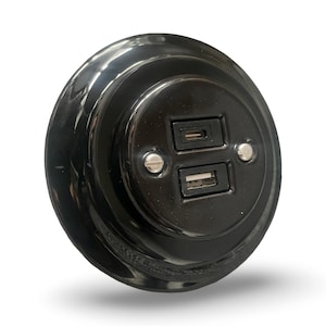 May include: A glossy black USB charger with a circular design. It features two ports: one USB-C and one USB-A, with two small silver screws. The charger is designed for convenient charging of electronic devices.