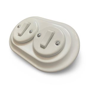 May include: A white double light switch with two rectangular toggle switches. The switch plate is oval-shaped and has a glossy finish. Each switch is secured with small silver screws.