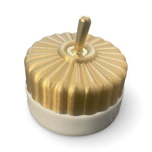 May include: A gold and white ceramic light switch with a brass knob. The switch has a decorative, fluted design.