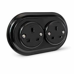 May include: A glossy black double electrical wall socket with an oval-shaped faceplate. The unit features two standard three-pin socket configurations, each secured with two visible silver-coloured metal screws on the front surface.