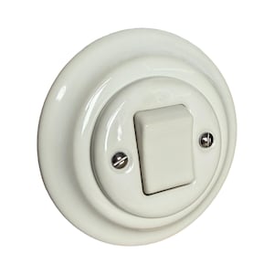 May include: Cream-colored, round light switch with a rectangular toggle. The switch has a glossy finish and is mounted with two small screws. The design is simple and classic, suitable for various interior styles.