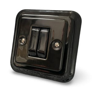 Puede incluir: Un interruptor doble negro brillante con dos interruptores basculantes rectangulares. La placa del interruptor es cuadrada con esquinas redondeadas y dos tornillos pequeños. Un diseño clásico y vintage.