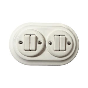 Peut inclure: Un interrupteur double blanc avec deux ensembles d'interrupteurs rectangulaires. Les interrupteurs sont encastrés dans une plaque ovale arrondie. Chaque interrupteur est fixé avec de petites vis.
