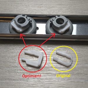 Könnte beinhalten: Das Bild zeigt zwei graue Kunststoffkomponenten mit weißen Einsätzen, die auf einer Metallschiene montiert sind. Darunter hebt ein roter Kreis ein weißes "Optimiert!" Kunststoffteil hervor, und ein gelber Kreis zeigt das "Original"-Teil.
