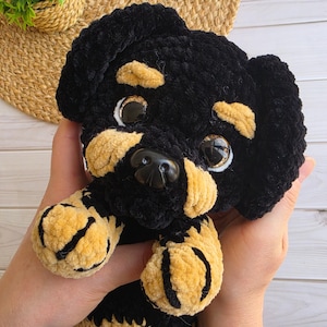 Könnte beinhalten: Ein handgefertigtes Häkel-Plüschtier eines Rottweiler-Welpen aus weichem, schwarzem und beigefarbenem Samtgarn. Das Spielzeug hat große, glänzende braune Sicherheitsaugen, eine schwarze Kunststoffnase und markante beige Abzeichen über den Augen.