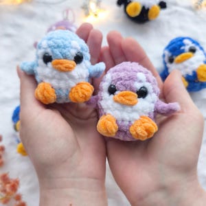 May include: Handmade crochet penguin toys in various colors, including blue, purple, and black. Each penguin has a white belly, orange feet, and black eyes. The penguins are small and plush, perfect for a child's toy collection.