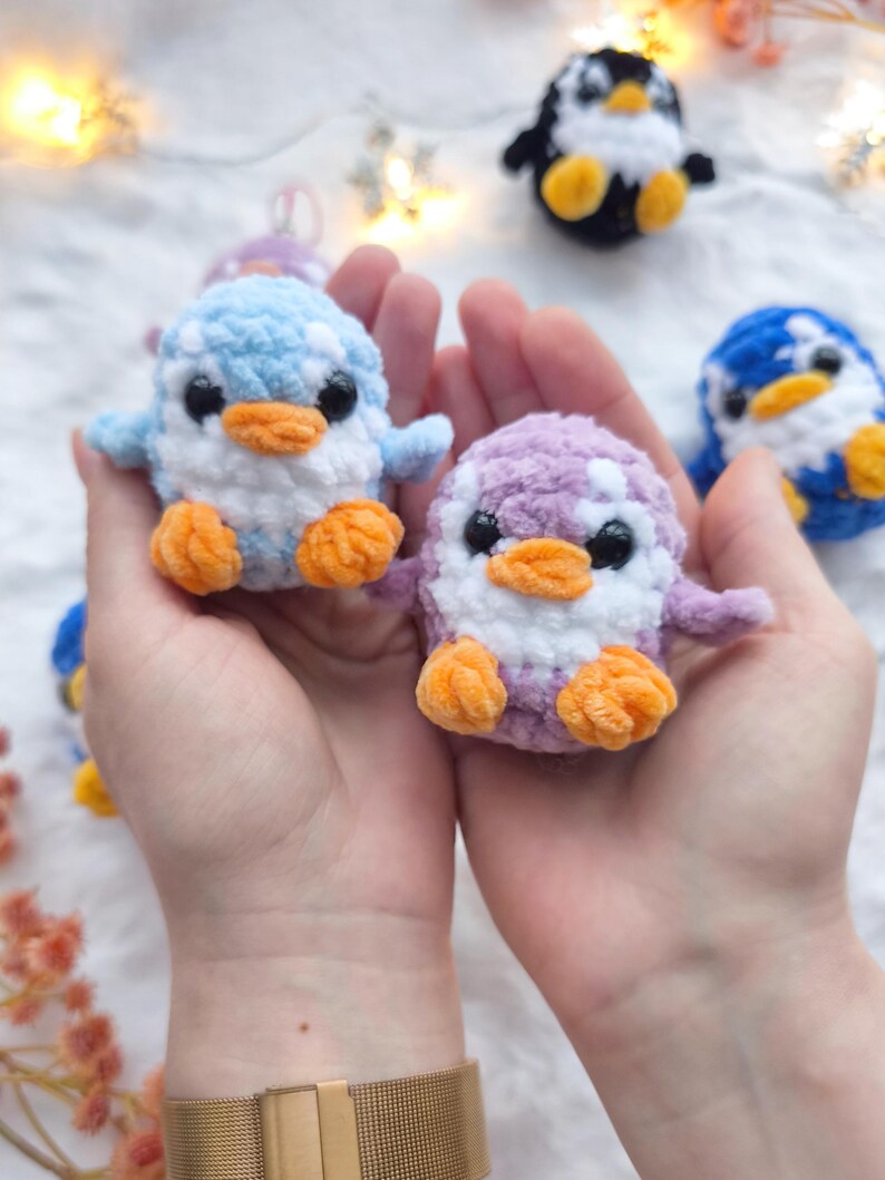 May include: Handmade crochet penguin toys in various colors, including blue, purple, and black. Each penguin has a white belly, orange feet, and black eyes. The penguins are small and plush, perfect for a child's toy collection.