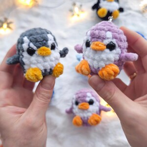 May include: Handmade crochet penguin ornaments in various colors: gray, purple, and black. Each penguin has a white belly, orange feet and beak, and black eyes. These small, plush penguins are perfect for holiday decorations or as a cute gift.
