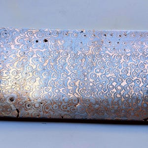 May include: A rectangular metal plate with a swirling pattern in silver, copper, and brown. The surface has a textured appearance with small holes. The plate is likely a decorative or functional item, possibly for crafting.