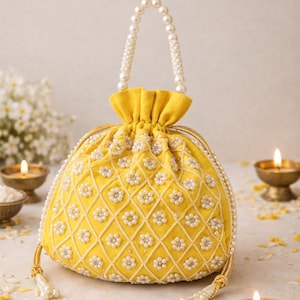 以下が含まれることがあります： パールハンドルと白い花のビーズ細工が施された黄色の巾着バッグ。バッグはダイヤモンド模様とゴールドのアクセントが特徴です。ハンドルはパール製です。バッグは白い表面に置かれています。