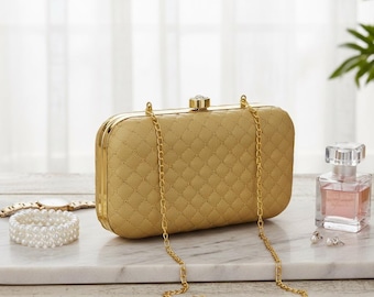 May include: A gold quilted clutch with a chain strap, a pearl bracelet, a watch, and a bottle of perfume. The clutch has a diamond pattern and a jeweled clasp. The perfume bottle is square and clear.