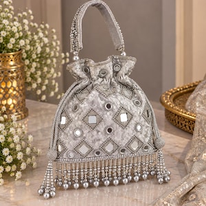 May include: A silver-toned drawstring handbag featuring a geometric pattern of square mirrors and intricate beadwork. The bag includes a single top handle, a cinched top closure, and a bottom fringe composed of dangling silver beads and pearls.