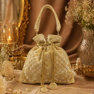 May include: A gold-colored, drawstring pouch bag with a handle. The bag is made of a soft, quilted fabric and is embellished with intricate gold embroidery. The bag has a round, beaded tassel at the end of the drawstring.