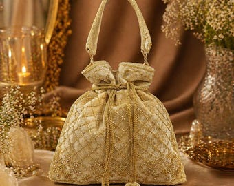 May include: A gold-colored, drawstring pouch bag with a handle. The bag is made of a soft, quilted fabric and is embellished with intricate gold embroidery. The bag has a round, beaded tassel at the end of the drawstring.