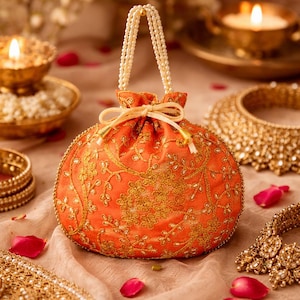 Könnte beinhalten: Eine orangefarbene, bestickte Tasche mit Perlenhenkel und Kordelverschluss. Die Tasche ist mit goldenen Blumenstickereien verziert und von Goldschmuck und Rosenblättern umgeben.