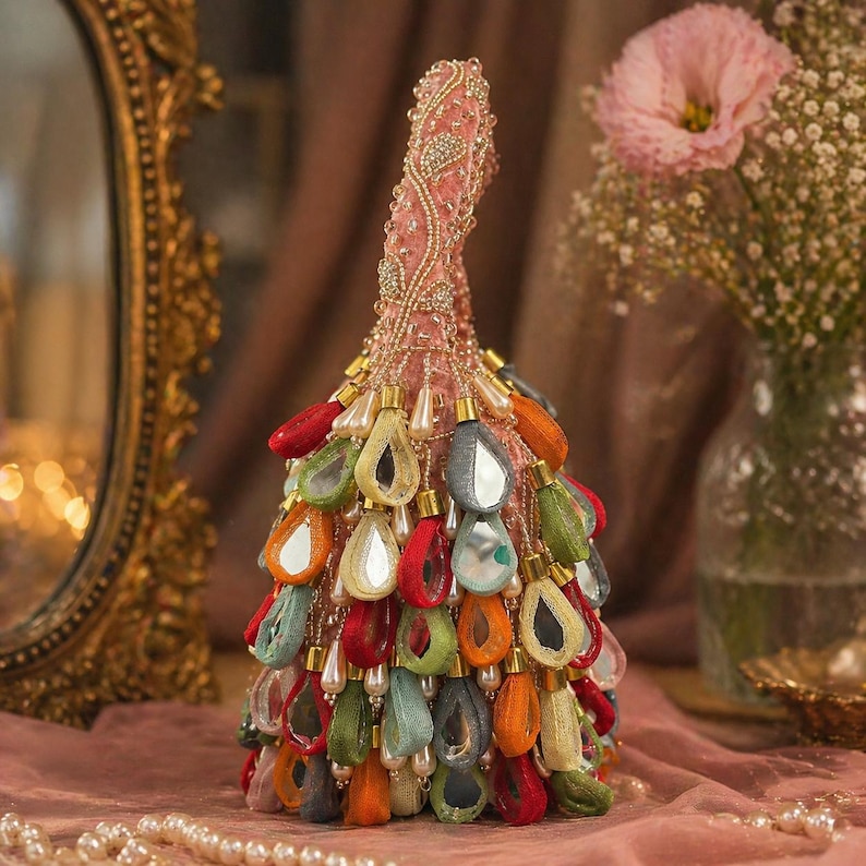 May include: A pink fabric handbag featuring a tall, tapered silhouette adorned with intricate beadwork and numerous dangling, teardrop-shaped fabric charms in vibrant colors like red, orange, green, and blue, each containing a small mirror.