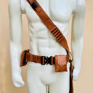 Peut inclure: Ensemble de ceinture utilitaire et bandouli&egrave;re en cuir marron. La ceinture est dot&eacute;e d'une boucle noire et de plusieurs pochettes. La bandouli&egrave;re a une boucle noire et une s&eacute;rie de boucles. Une sangle de jambe est &eacute;galement incluse.