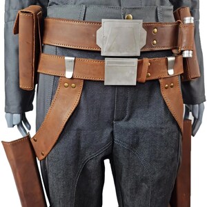May include: A costume detail showing a grey jumpsuit with brown leather elements. It features a double belt with silver buckles, pouches, and leg holsters. The leather has a worn appearance, and the jumpsuit has visible stitching details.