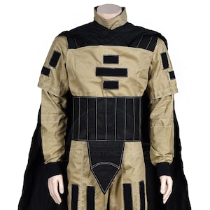 Puede incluir: Un disfraz negro y marr&oacute;n con una capa negra y un dise&ntilde;o geom&eacute;trico en el pecho. El disfraz tiene un cintur&oacute;n negro y detalles negros en los brazos y las piernas.