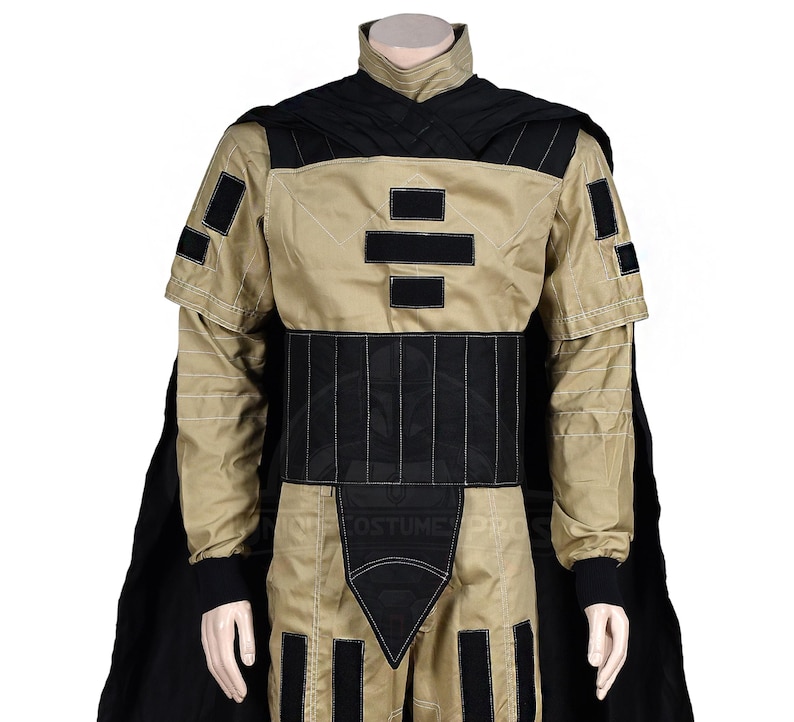 Puede incluir: Un disfraz negro y marr&oacute;n con una capa negra y un dise&ntilde;o geom&eacute;trico en el pecho. El disfraz tiene un cintur&oacute;n negro y detalles negros en los brazos y las piernas.