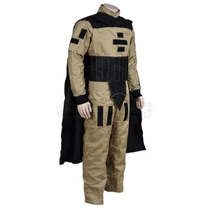 Puede incluir: Un mono beige con detalles negros y una capa negra. El mono tiene un cintur&oacute;n negro y formas geom&eacute;tricas negras en el pecho y las piernas.