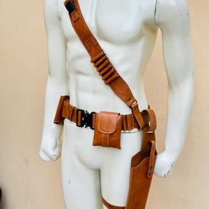 Peut inclure: Ensemble de ceinture et d'&eacute;tui utilitaire en cuir marron. L'ensemble comprend une bandouli&egrave;re avec des boucles pour cartouches, une ceinture avec une pochette et une sangle de jambe avec un &eacute;tui. Le cuir est de couleur marron moyen avec des coutures visibles et du mat&eacute;riel m&eacute;tallique.
