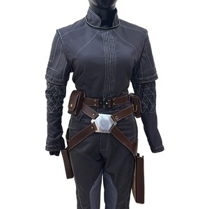 Puede incluir: Una chaqueta gris oscuro con costuras blancas y un cintur&oacute;n de cuero marr&oacute;n con una hebilla plateada. La chaqueta tiene cuello y mangas largas. El cintur&oacute;n tiene una funda a cada lado.