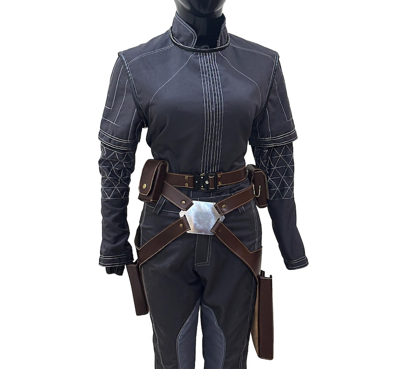 Puede incluir: Una chaqueta gris oscuro con costuras blancas y un cintur&oacute;n de cuero marr&oacute;n con una hebilla plateada. La chaqueta tiene cuello y mangas largas. El cintur&oacute;n tiene una funda a cada lado.