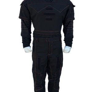 K&ouml;nnte beinhalten: Schwarzer Overall mit roten Steppn&auml;hten. Das Outfit hat einen hohen Kragen, Schulterakzente und rechteckige Patches auf Brust und Beinen. Das lang&auml;rmlige Oberteil und die Hose sind mit sichtbaren roten N&auml;hten versehen.