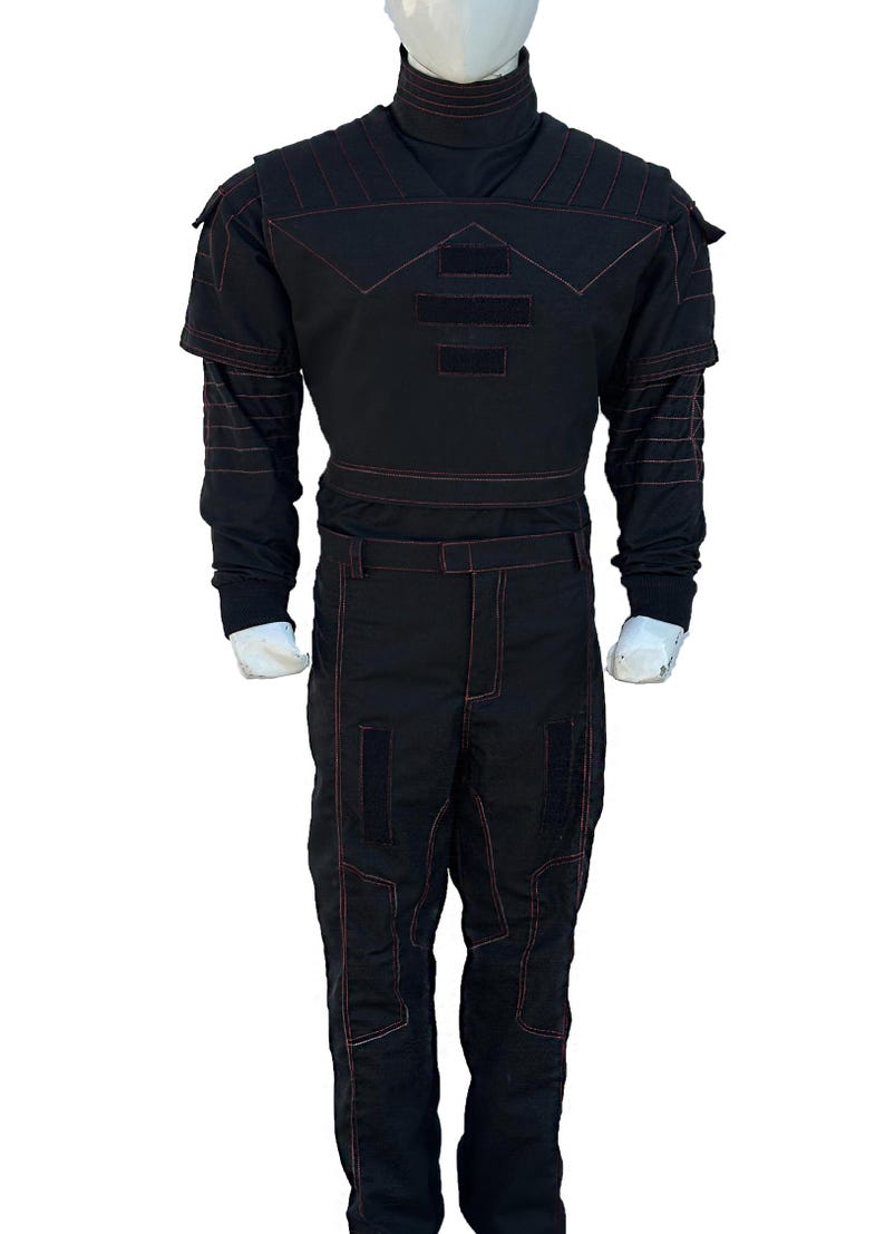 K&ouml;nnte beinhalten: Schwarzer Overall mit roten Steppn&auml;hten. Das Outfit hat einen hohen Kragen, Schulterakzente und rechteckige Patches auf Brust und Beinen. Das lang&auml;rmlige Oberteil und die Hose sind mit sichtbaren roten N&auml;hten versehen.
