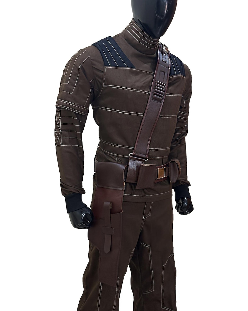 Pu&ograve; includere: Un costume marrone con cuciture bianche, con un top a collo alto, pantaloni e una cintura multiuso con tasche. Il costume include una tracolla e guanti neri. Il manichino &egrave; su sfondo bianco.