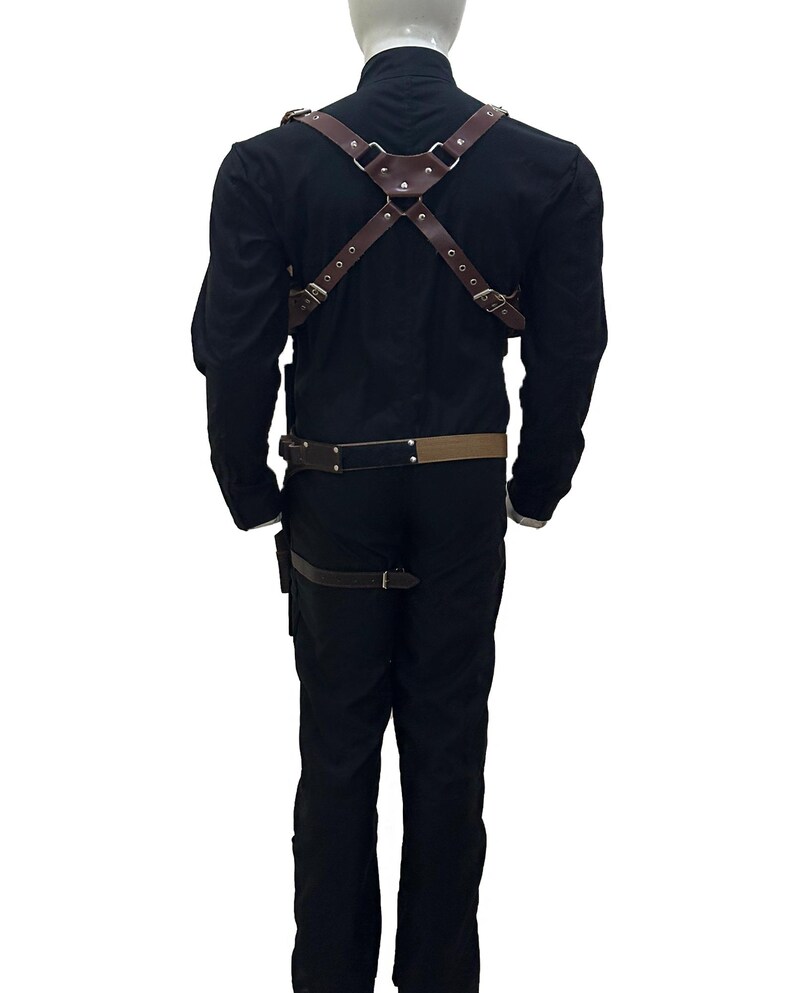 May include: Brown leather harness with adjustable straps and metal hardware. The harness is worn over a black long-sleeve shirt and pants. A matching belt and leg strap are also visible. The outfit is displayed on a mannequin.